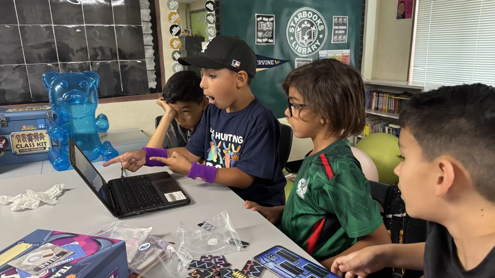 Four boys around a laptop and class kit box, one pointing excitedly at the screen